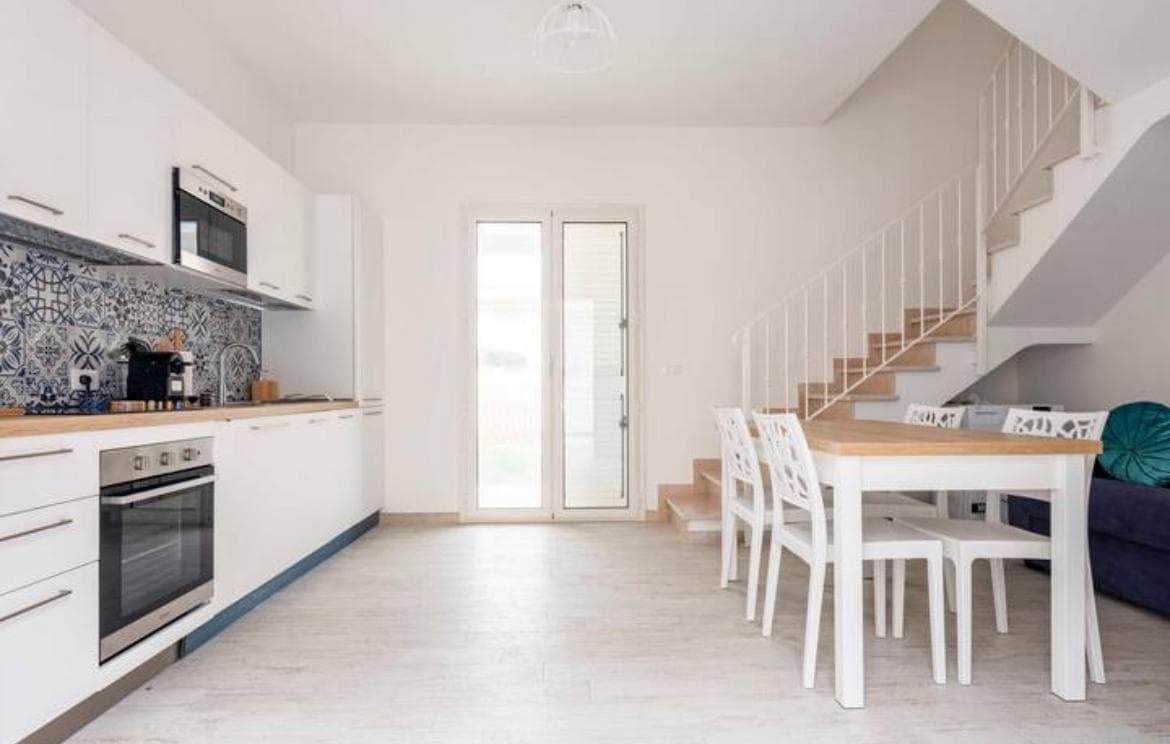Soggiorno con cucina, tavolo bianco e scala che porta al piano di sopra