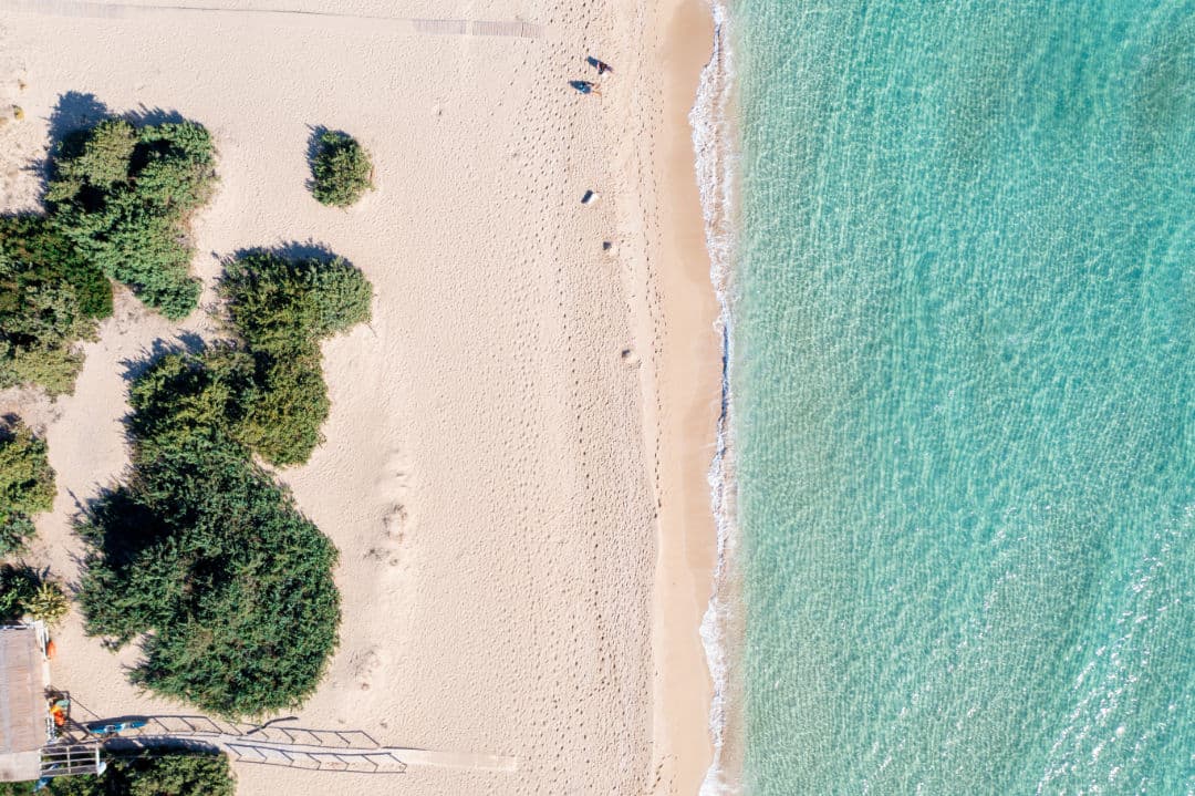 Spiaggia vista dall'alto: sabbia chiara, macchia verde e mare turchese