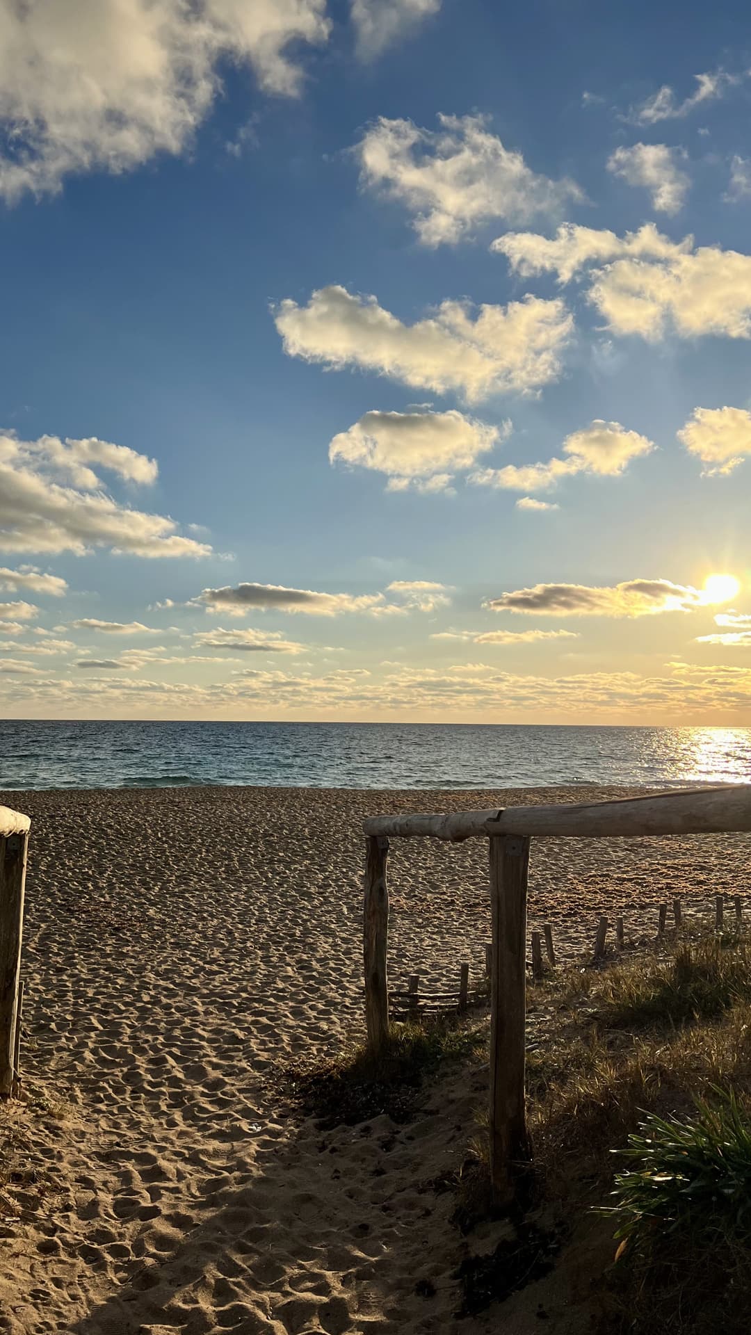 Passerella di legno che scende sulla spiaggia, con il sole basso sul mare